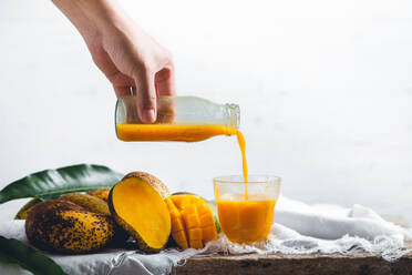 Cropped Hand Gießen Mango-Saft aus der Flasche in Glas gegen weißen Hintergrund - EYF05779