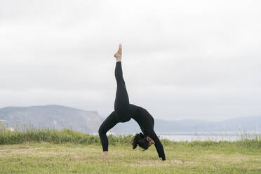Flexible junge Frau übt Yoga auf Gras gegen den Himmel - MTBF00437