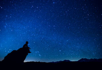 Silhouette Mann sitzt auf Felsen gegen Konstellation im blauen Himmel - EYF05800