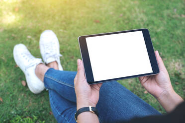Niedriger Ausschnitt einer Frau, die ein digitales Tablet hält, während sie auf einem Feld sitzt - EYF05937