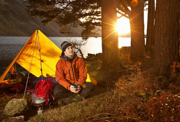 Man enjoying hot drink at simple camp in the British Lake district - CAVF85304