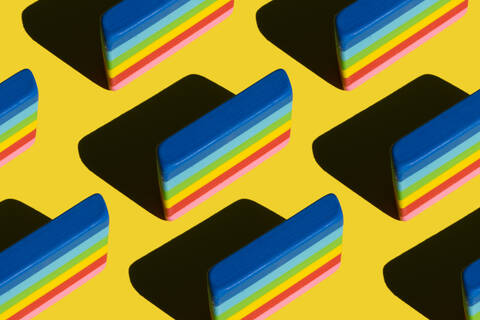 Muster aus regenbogenfarbenen Radiergummis vor gelbem Hintergrund, lizenzfreies Stockfoto