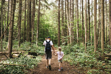 Man holding hands of daughter while hiking in woodland - JVSF00011