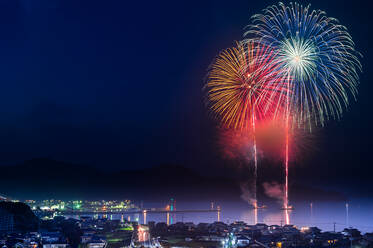 Feuerwerk über dem See bei beleuchteter Stadt in der Nacht - EYF05968