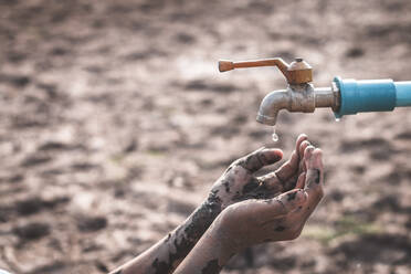 Cropped Schmutzige Hände der Person unter dem Wasserhahn auf kargen Land während der Dürre - EYF06035