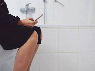 Midsection Of Woman Using Phone While Sitting In Toilet - EYF06077