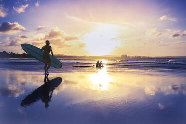 Full Length Of Man Walking With Surfboard By Silhouette People Sitting At Beach - EYF06118