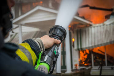Nahaufnahme von einem Feuerwehrmann Spritzen brennenden Haus mit Schlauch - EYF06135