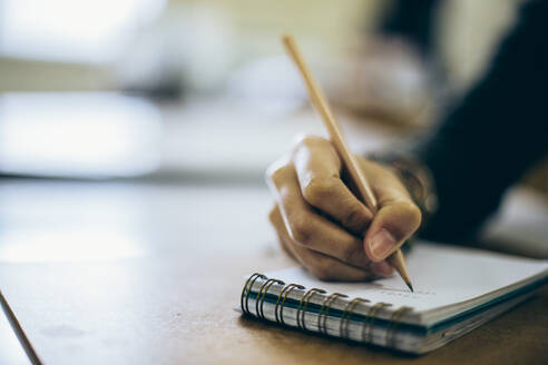 Abgeschnittene Hand einer Studentin, die auf einem Notizblock auf dem Schreibtisch schreibt - EYF06148