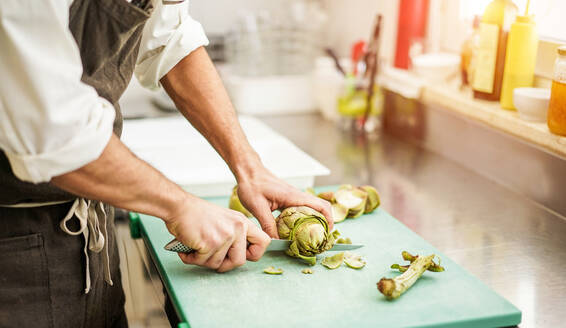 Midsection Of Man Cutting Artichoke In Kitchen - EYF06199