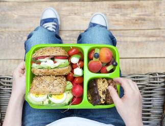 Niedriger Ausschnitt einer Person mit Lunchbox auf Korbstuhl sitzend - EYF06299