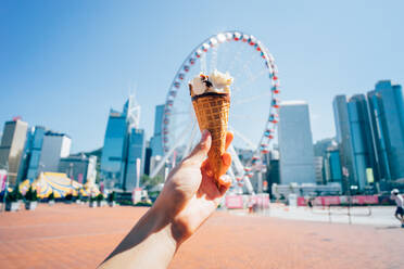 Cropped Image Of Hand Holding Ice Cream Against Ferris Wheel In City - EYF06459