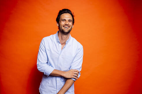 Cheerful handsome man standing against orange background - DAWF01604