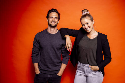 Smiling woman standing with hand on man's shoulder against orange background - DAWF01609