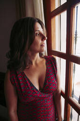 Beautiful woman thinking while looking through window at home - LJF01582