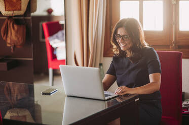 Lächelnde schöne Geschäftsfrau, die zu Hause arbeitet und einen Laptop im Wohnzimmer benutzt - LJF01586