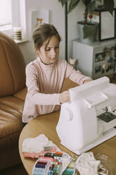 Girl sewing face mask in living room at home during coronavirus - VBF00093