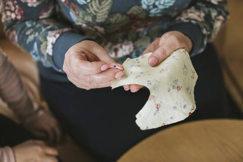 Mature woman holding straight pin and floral textile for sewing face mask at home stock photo