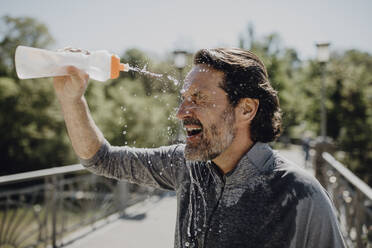 Nahaufnahme eines reifen Mannes, der sich Wasser ins Gesicht gießt, während er an einem sonnigen Tag im Park steht - JLOF00481