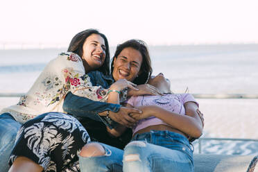 Mother and daughter laughing while embracing against sea - DCRF00302