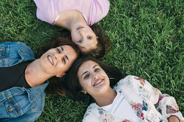 Smiling mother with daughters lying on grassy land in park - DCRF00318