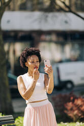 Mid adult woman applying lipstick while looking in smart phone - DCRF00320