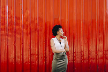 Stylish thoughtful woman looking away while standing against orange wall - DCRF00332