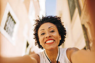 Nahaufnahme einer lächelnden erwachsenen Frau mit lockigem Haar vor einem Gebäude in einer Stadt - DCRF00337
