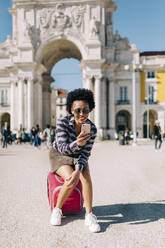 Woman taking selfie with smart phone while sitting against Praco Do Comercio, Lisbon, Portugal - DCRF00344