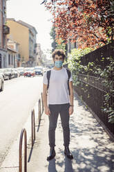 Junger Mann mit Gesichtsmaske auf dem Bürgersteig in der Stadt - MEUF00901