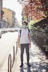 Young man wearing face mask while standing on sidewalk in city - MEUF00901