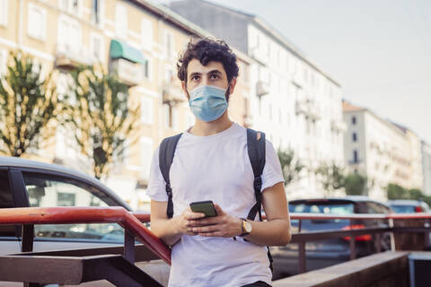 Junger Mann mit Maske, der in der Stadt steht und wegschaut, lizenzfreies Stockfoto