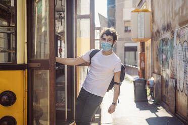 Young man wearing mask hanging on entrance of tram - MEUF00906