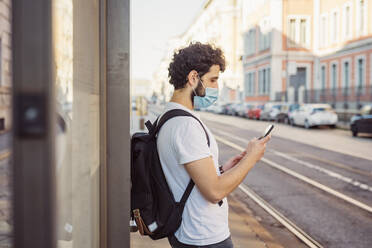 Man with backpack wearing mask while using mobile phone in city - MEUF00916