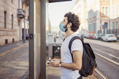 Young man wearing mask peeking through entrance of store - MEUF00917