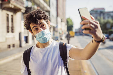 Close-up of young man wearing mask taking selfie with smart phone while standing in city - MEUF00921