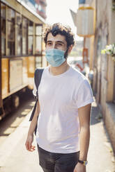 Young man wearing mask walking on city street during sunny day - MEUF00922