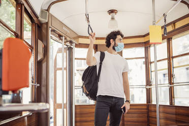 Young man wearing mask standing in tram - MEUF00925