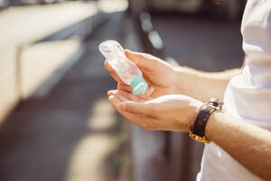 Close-up of young man washing hands with sanitizer while standing outdoors - MEUF00928