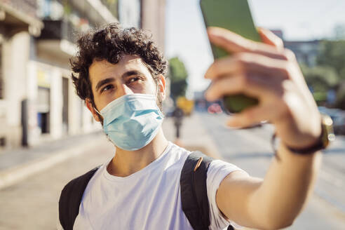 Close-up of man wearing face mask taking selfie with smart phone in city - MEUF00932