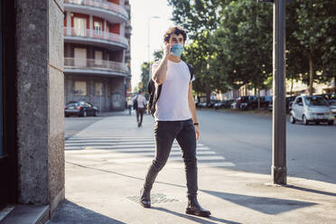 Man wearing face mask talking over smart phone while walking on street in city - MEUF00933