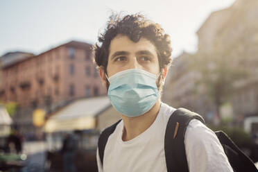 Close-up of thoughtful young man wearing face mask looking away in city - MEUF00934