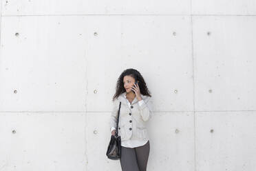 Stilvolle Geschäftsfrau im Gespräch über ein Smartphone, während sie an der Wand steht - JPTF00559