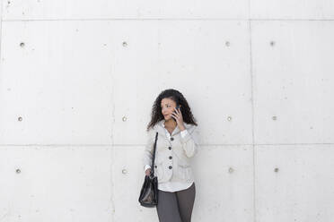 Stylish businesswoman talking over smart phone while standing against wall - JPTF00559