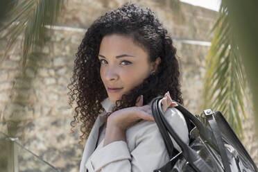 Close-up of stylish businesswoman holding purse while standing against wall - JPTF00565