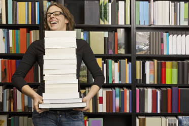 Woman carrying stack of books in bookstore - CAVF85509