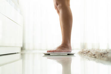 Low Section Of Woman Standing On Electronic Weight Scale On Floor - EYF06522