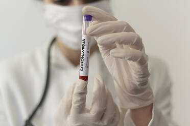 Mittelteil eines Wissenschaftlers, der ein Reagenzglas hält und eine Grippemaske auf dem Tisch trägt - EYF06535