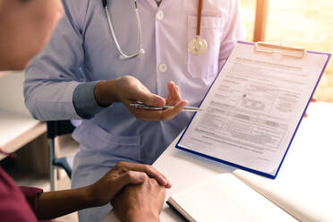 Midsection of Doctor Explaining Medical Insurance To Patient While Sitting On Table - EYF06571