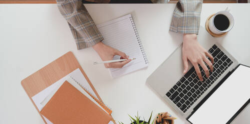 Hands Of Businesswoman Using Laptop While Writing In Diary At Office - EYF06589